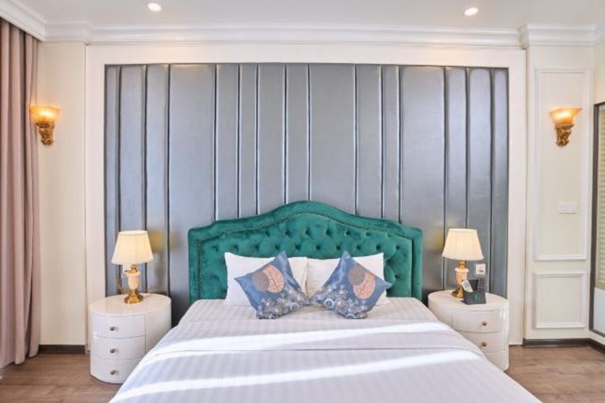Una habitación de hotel con cabecera capitonada, dos mesitas de noche con lámparas y una cama con ropa de cama a rayas.