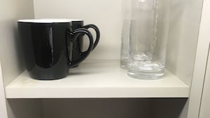 A shelf with black mugs and a clear glass, and below it, stacked white plates. - Olympic Park Large Balcony Near Shibuya (Setagaya)