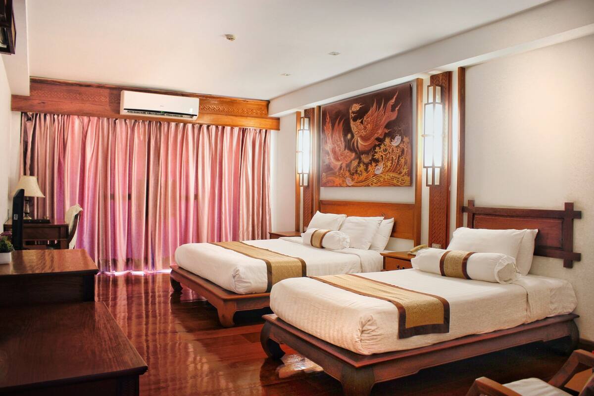 A hotel room with two beds, wooden furniture, a desk, and a large decorative painting on the wall.