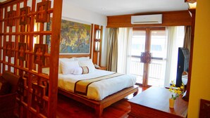 A hotel room with a bed, wooden floor, a desk with a chair, a television, and a window with curtains. - Chanthapanya Hotel (Vientiane)