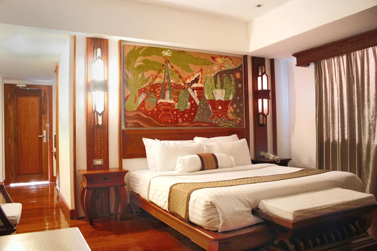 A hotel room with a large bed, a small bedside table, a nightstand, and a decorative wall hanging.