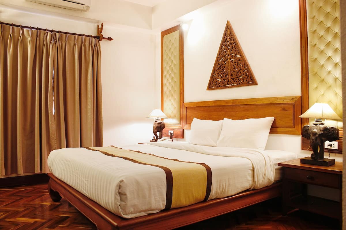 A hotel room with a wooden bed, a nightstand with lamps, a decorative wall panel, and a large window with curtains.