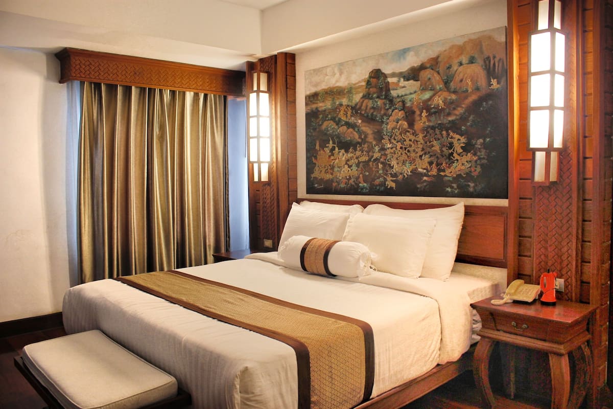 A hotel room with a large bed, a bench, a painting on the wall, and a nightstand with a telephone.
