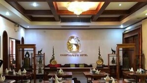 A hotel dining area with multiple tables and chairs, a chandelier, and a wall with the hotel's logo. - Chanthapanya Hotel (Vientiane)