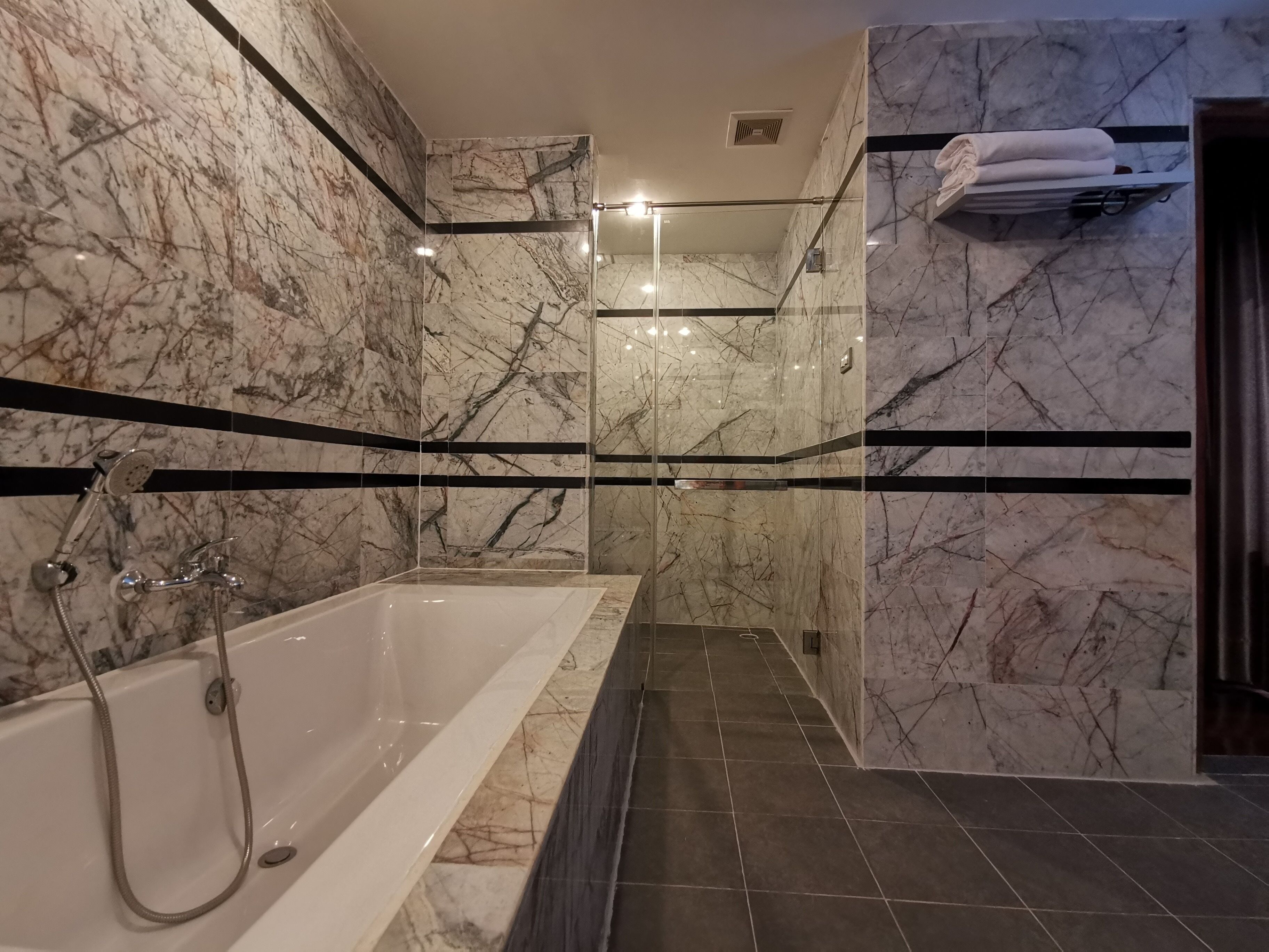 Ein modernes Badezimmer mit Marmorwand, einer Glaskabine für die Dusche und einer Badewanne.