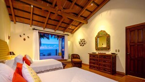 Un dormitorio con dos camas, techo de madera, un espejo grande y vista al mar.