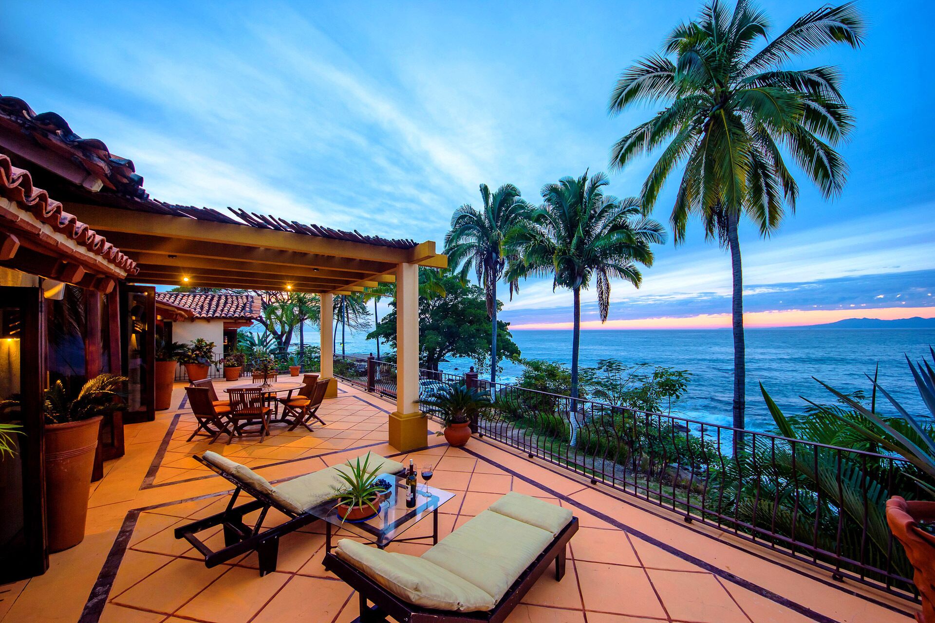 Una terrazza con vista sull'oceano, palme e un edificio con tetto in tegole.