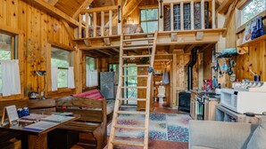 A wooden cabin interior with a loft bedroom, a dining area, and a kitchen. - Wizard's LOTR Cabin: New Treehouse Addition! Pet-friendly.  (Holdingford)