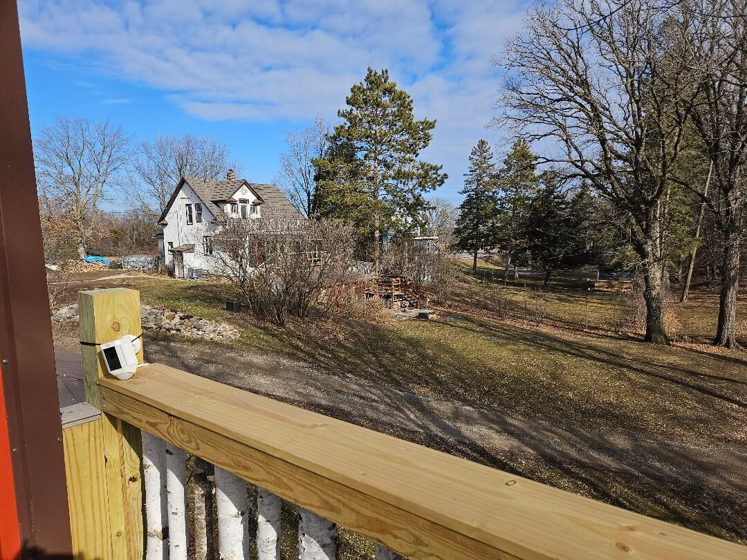 En träveranda med ett vitt staket, ett hus i bakgrunden och en klar himmel.