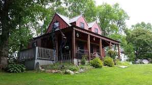 A red wooden house with a porch, surrounded by a grassy yard and trees. - Wizard's LOTR Cabin: New Treehouse Addition! Pet-friendly.  (Holdingford)