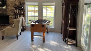 A cozy room with a foosball table, stone wall, large windows, and a wooden cabinet. - Hideaway @ Knob Hill (Little Elm)