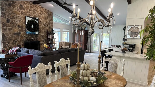 A spacious living room with a stone fireplace, a large sofa, and a dining area with a wooden table set with placemats and candles. - Hideaway @ Knob Hill (Little Elm)