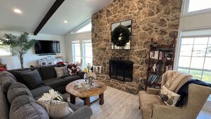 A cozy living room with a stone wall, a fireplace, a television, and a bookshelf. - Hideaway @ Knob Hill (Little Elm)