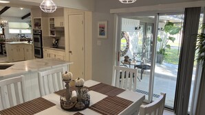 A modern kitchen with white cabinetry, a dining area with a white table and brown placemats, and a view of the outdoors through glass doors. - Hideaway @ Knob Hill (Little Elm)