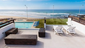 Una terraza en la azotea con piscina, sillas de descanso y vistas al océano.
