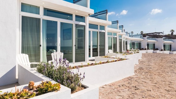 Una hilera de villas modernas frente a la playa, con amplios ventanales de vidrio, paredes blancas y zonas de estar al aire libre.