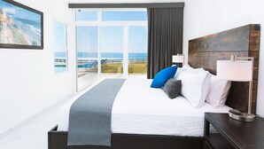 Un dormitorio con una cama grande, vistas al océano y un balcón con piscina y sillones de descanso.