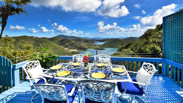 A dining area with a table set for four, overlooking a scenic landscape with hills and a body of water. - Beautiful Cottage w/Stunning View, Backup Power, Hot Tub, Family or 2 Couples  (Coral Bay)