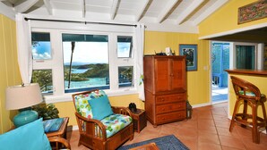 A cozy living room with a view of the sea, a wooden cabinet, and a dining area. - Beautiful Cottage w/Stunning View, Backup Power, Hot Tub, Family or 2 Couples  (Coral Bay)