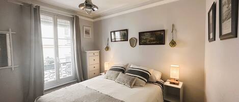 A bedroom with a bed, bedside tables, a dresser, a window with curtains, and wall-mounted artwork.