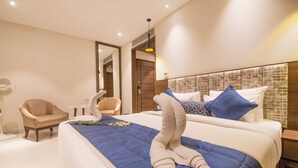 A hotel room with a large bed, a chair, a small table, and a mirror. - Hotel Sumaditya (Jaipur)