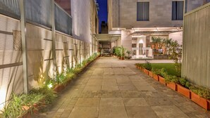 A narrow, paved courtyard with potted plants lining the sides, leading to a building entrance. - Hotel Sumaditya (Jaipur)