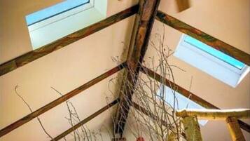 Ein Zimmer mit schrägen Wänden, freiliegenden Holzbalken und einem Deckenventilator. Es gibt Dachfenster und ein rundes Fenster in der Decke.