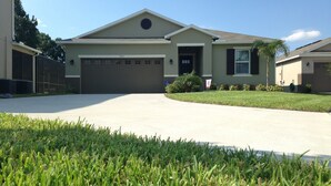 A single-story house with a garage, a well-maintained lawn, and a clear sky. - 5 Stars House With WiFi, Game Room, Private Heated Spa & Pool In a Gated Area (Kissimmee)