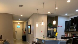A modern kitchen with a central island, bar stools, and a pizza sign. - 5 Stars House With WiFi, Game Room, Private Heated Spa & Pool In a Gated Area (Kissimmee)