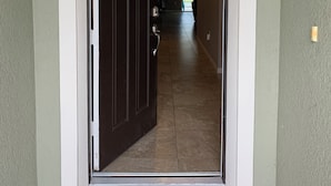 A hallway with a dark wooden door, a hanging wreath, and a ceiling light. - 5 Stars House With WiFi, Game Room, Private Heated Spa & Pool In a Gated Area (Kissimmee)