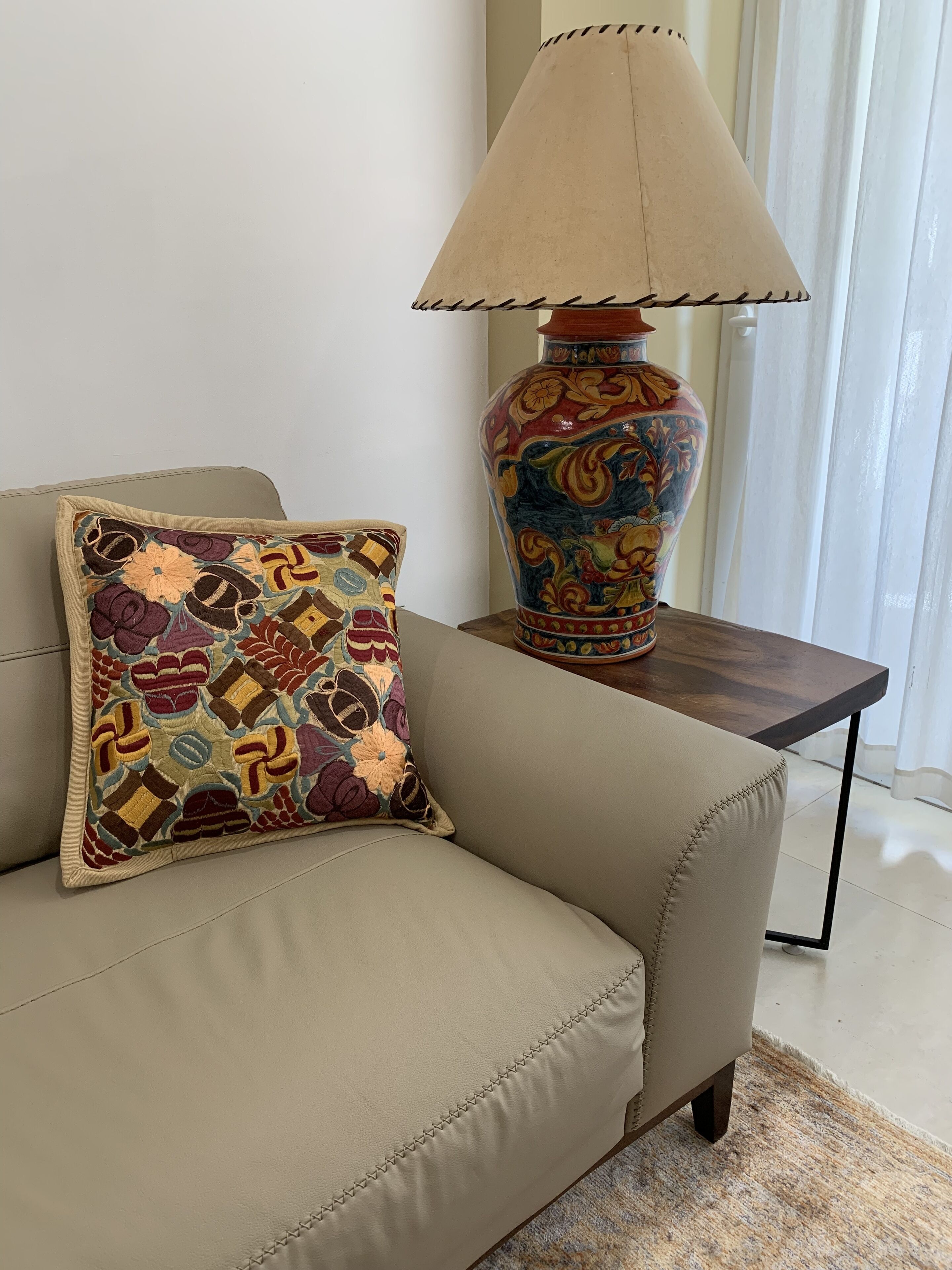 A beige sofa with a colorful embroidered pillow, a decorative vase, and a table lamp.