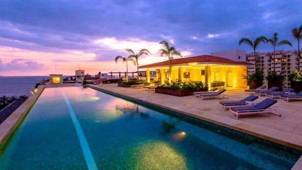 A poolside area with lounge chairs and a building with a red roof.