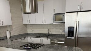 A modern kitchen with white cabinets, a stainless steel range hood, a built-in microwave, and a refrigerator with a water dispenser.