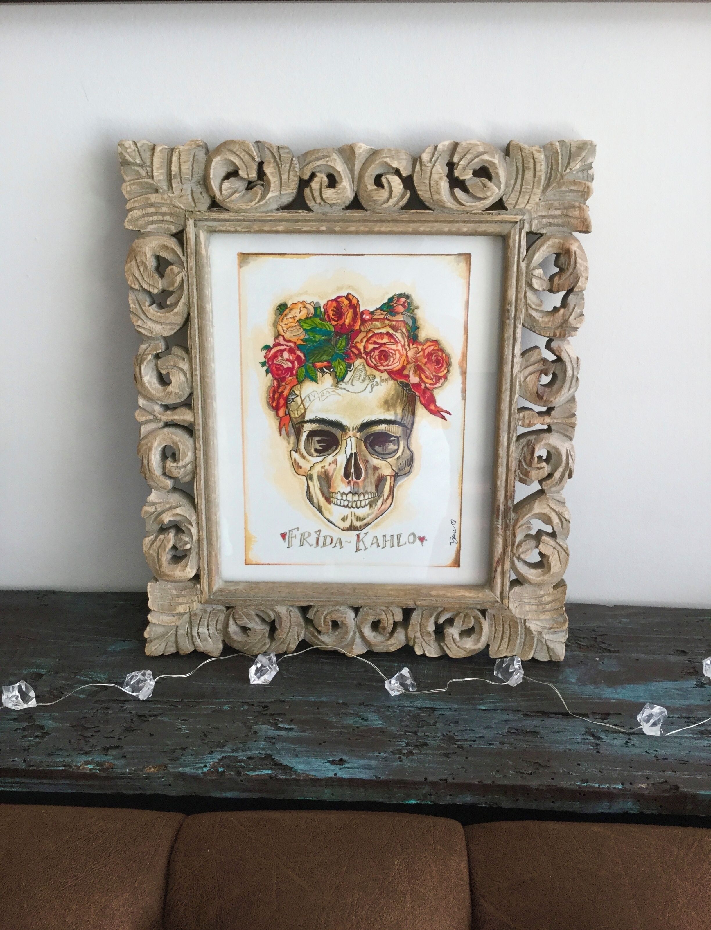 A framed artwork with a skull and floral design, displayed on a dark wooden surface.