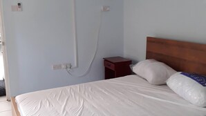 Ein Schlafzimmer mit einem Bett, einem Holz-Kopfteil, einem Nachttisch, einer Wand-Klimaanlage und einem Deckenventilator.