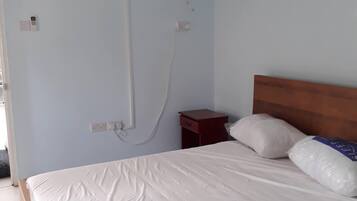 Un dormitorio con cama, cabecera de madera, mesita de noche, aire acondicionado de pared y ventilador de techo.