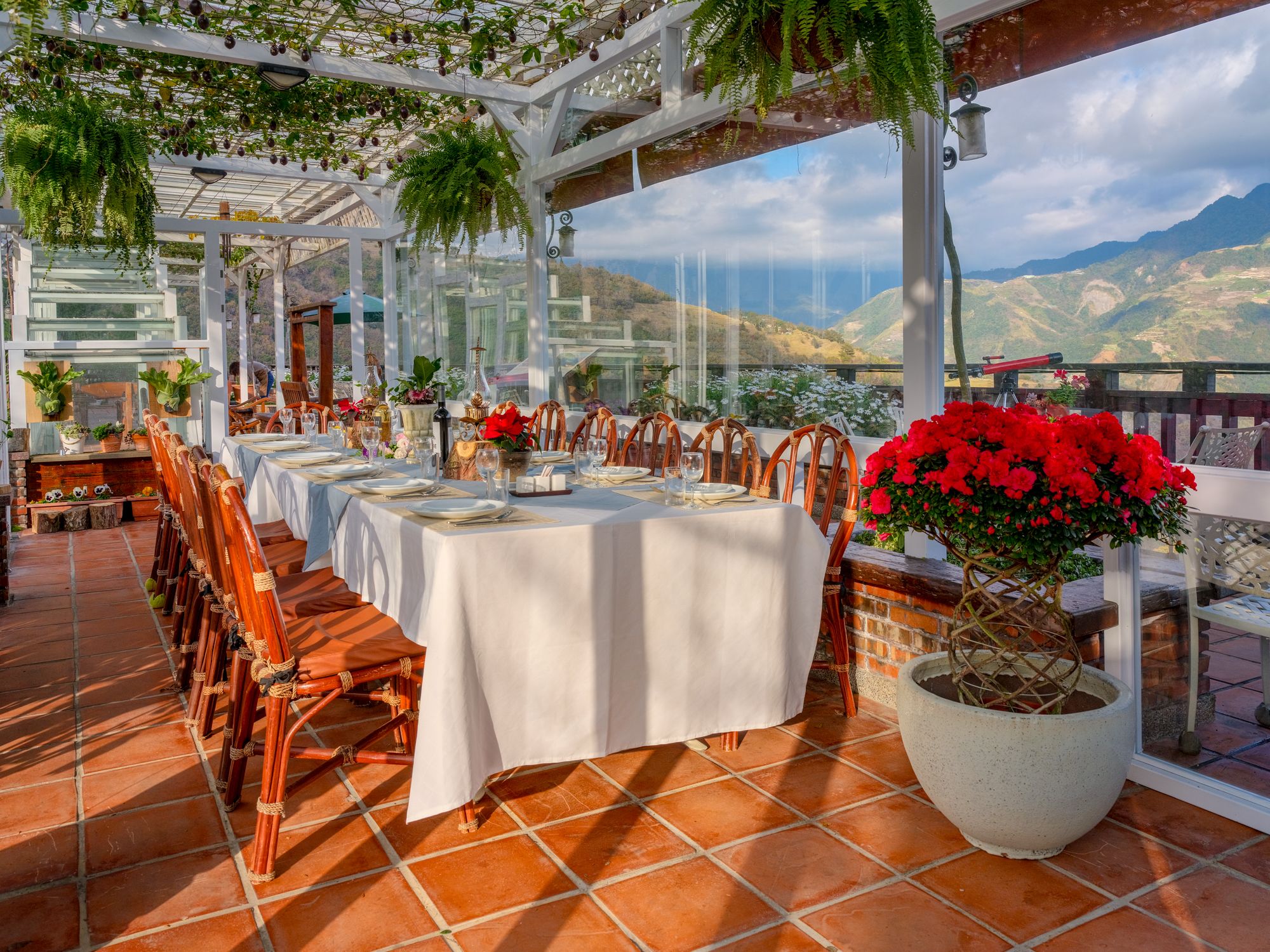 An outdoor dining area with white tables and chairs, surrounded by a white pergola with hanging plants.