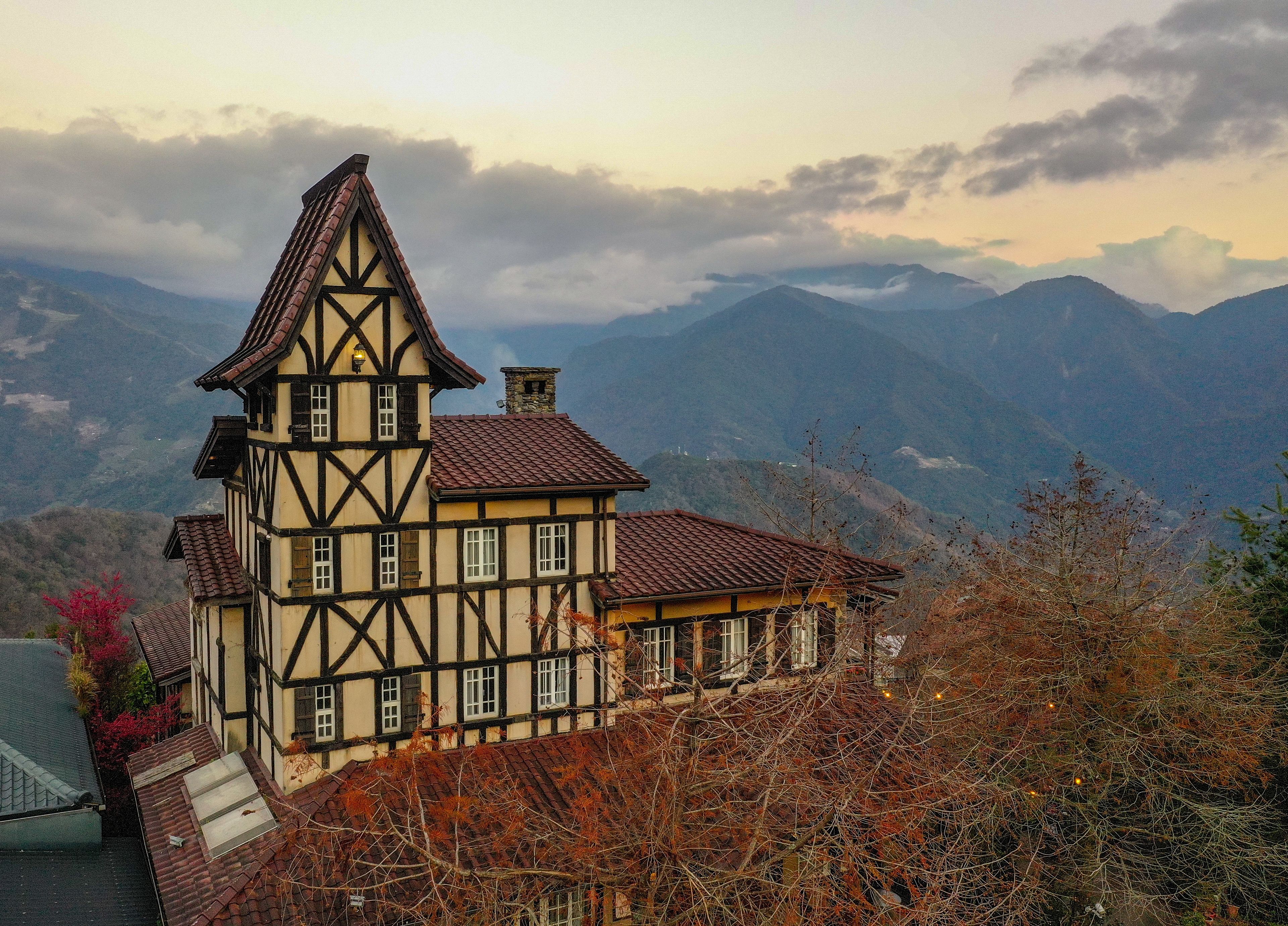 A traditional half-timbered house with a steep gabled roof, set against a mountainous backdrop.