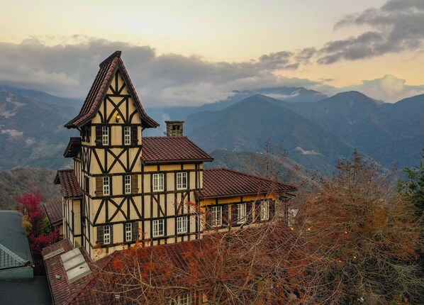 A traditional half-timbered house with a steep gabled roof, set against a mountainous backdrop. - Oncoming Luck Villa (Ren'ai)