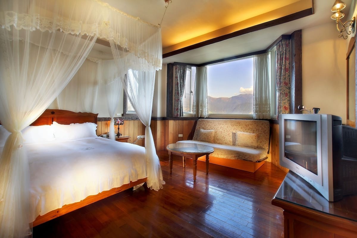 Quarto com cama de dossel, televisão, sofá e vista para montanhas pela janela.