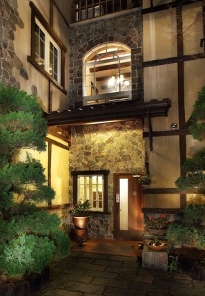 A stone facade with a wooden door, potted plants, and a stone bench. - Oncoming Luck Villa (Ren'ai)