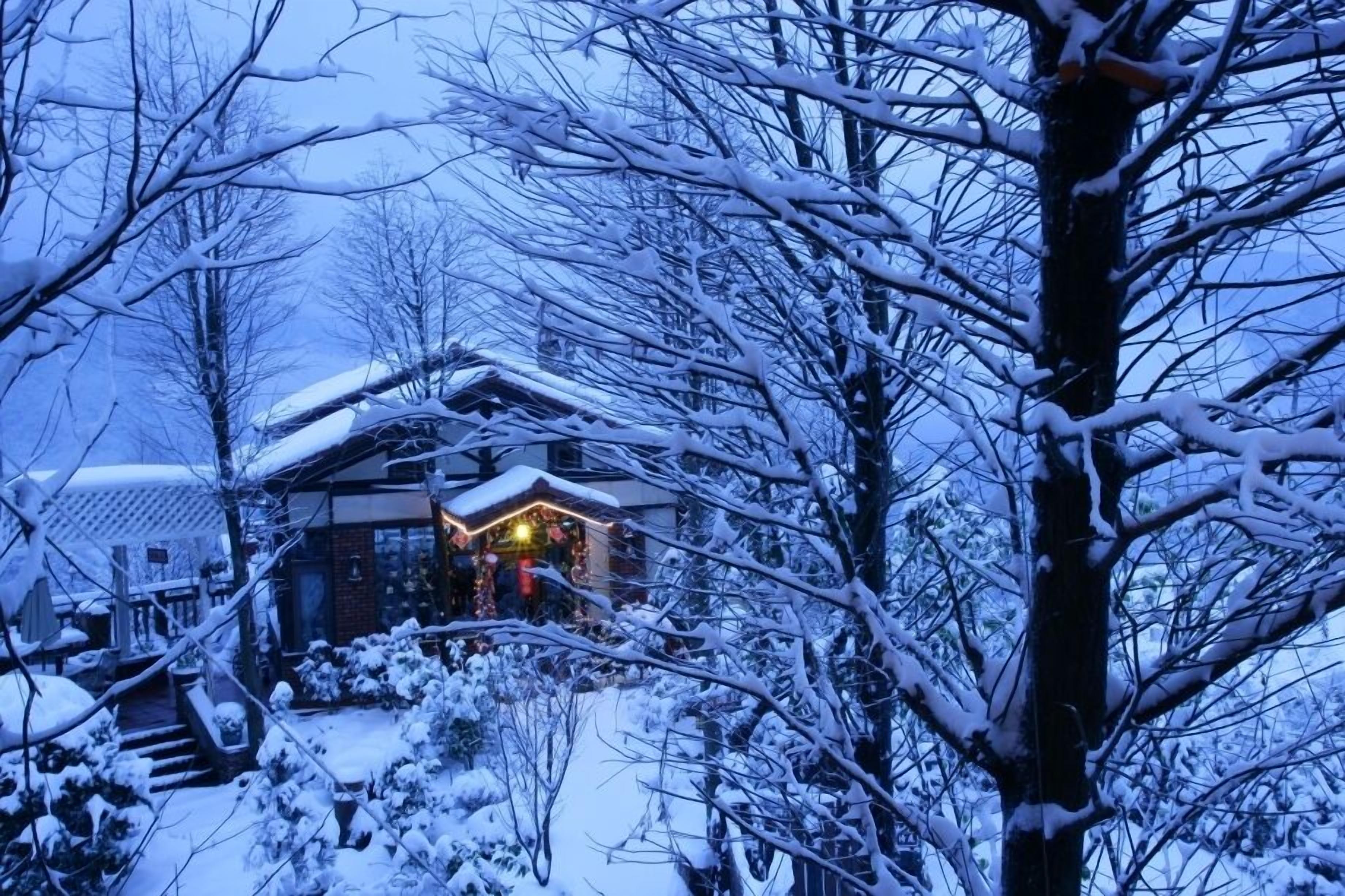 Un paisaje cubierto de nieve con una casa que tiene una entrada iluminada y una escalera visible que lleva a la puerta.