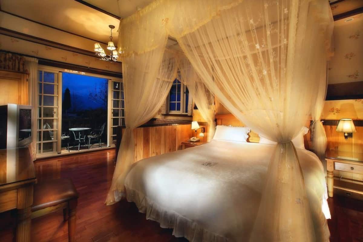 Quarto com cama de dossel, piso de madeira, uma grande janela com vista e um candelabro.