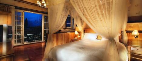 Un dormitorio con cama con dosel, suelo de madera, un ventanal con vistas y una araña.