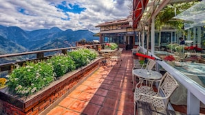 Um terraço com área de estar ao ar livre, vista para montanhas e um espaço de refeições envidraçado.