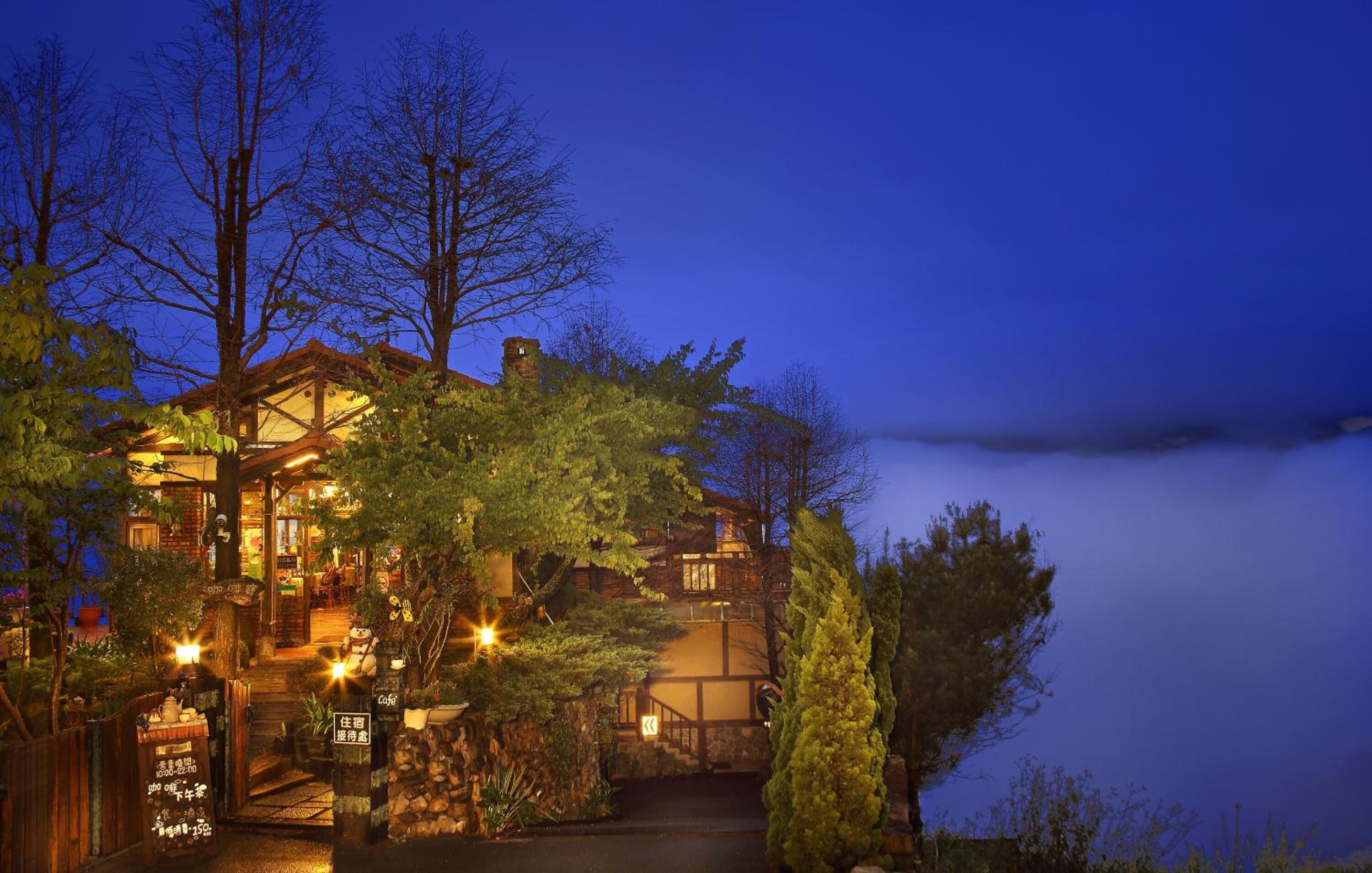 A traditional wooden building with a staircase leading to a second floor, surrounded by trees and a view of the sky.