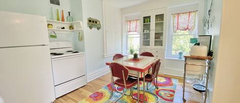 A compact kitchen with white appliances, a dining table with red chairs, and a colorful rug.