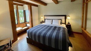 A bedroom with a large bed, wooden beams, a bench by the window, and two bedside lamps.