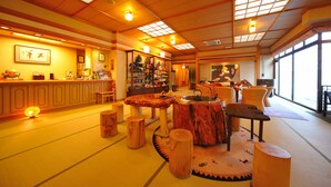 Een traditioneel Japans verblijf met tatami vloerbedekking, houten meubels en een receptie met een balie en planken vol objecten.
