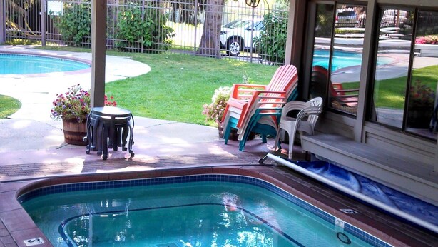 A swimming pool with a covered patio area, a lawn, and a fenced yard.